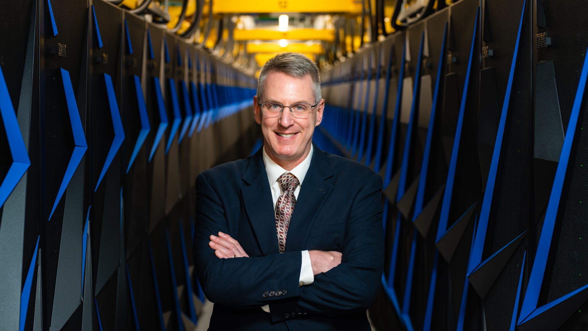Portrait of Phil Roth standing between cabinets of the Summit supercomputer