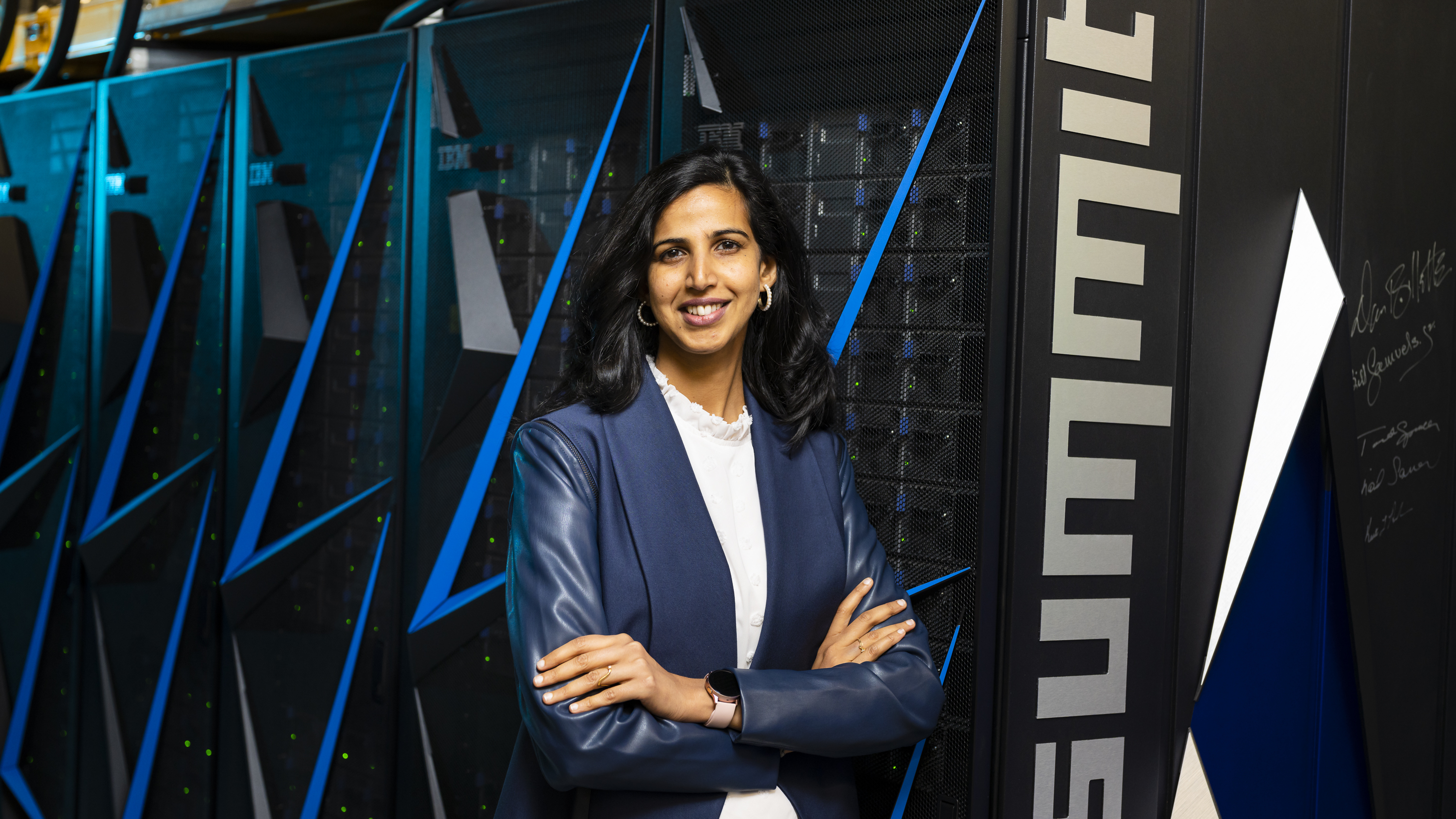 A woman stands in front of the Summit supercomputer
