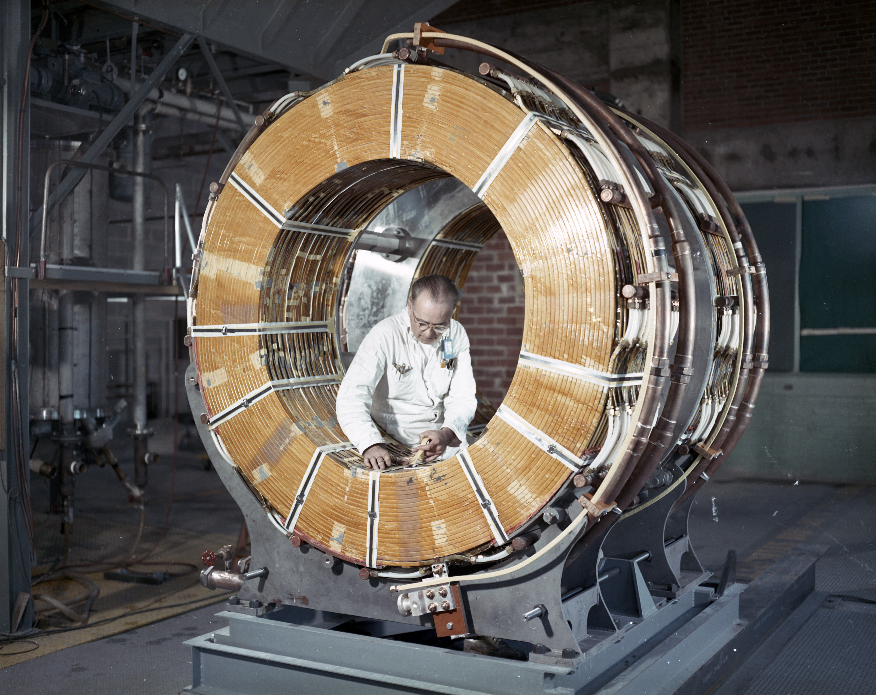 A man kneeling in the middle a very large metal magnet coil, performing maintenance work