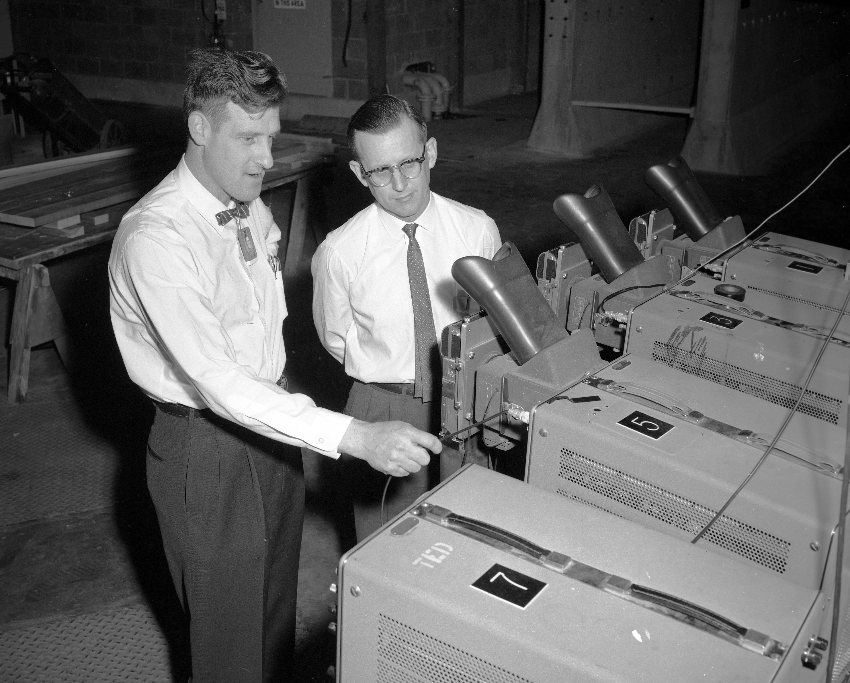 A black and white photo of two researchers looking into a viewport of a machine used in a fusion experiment