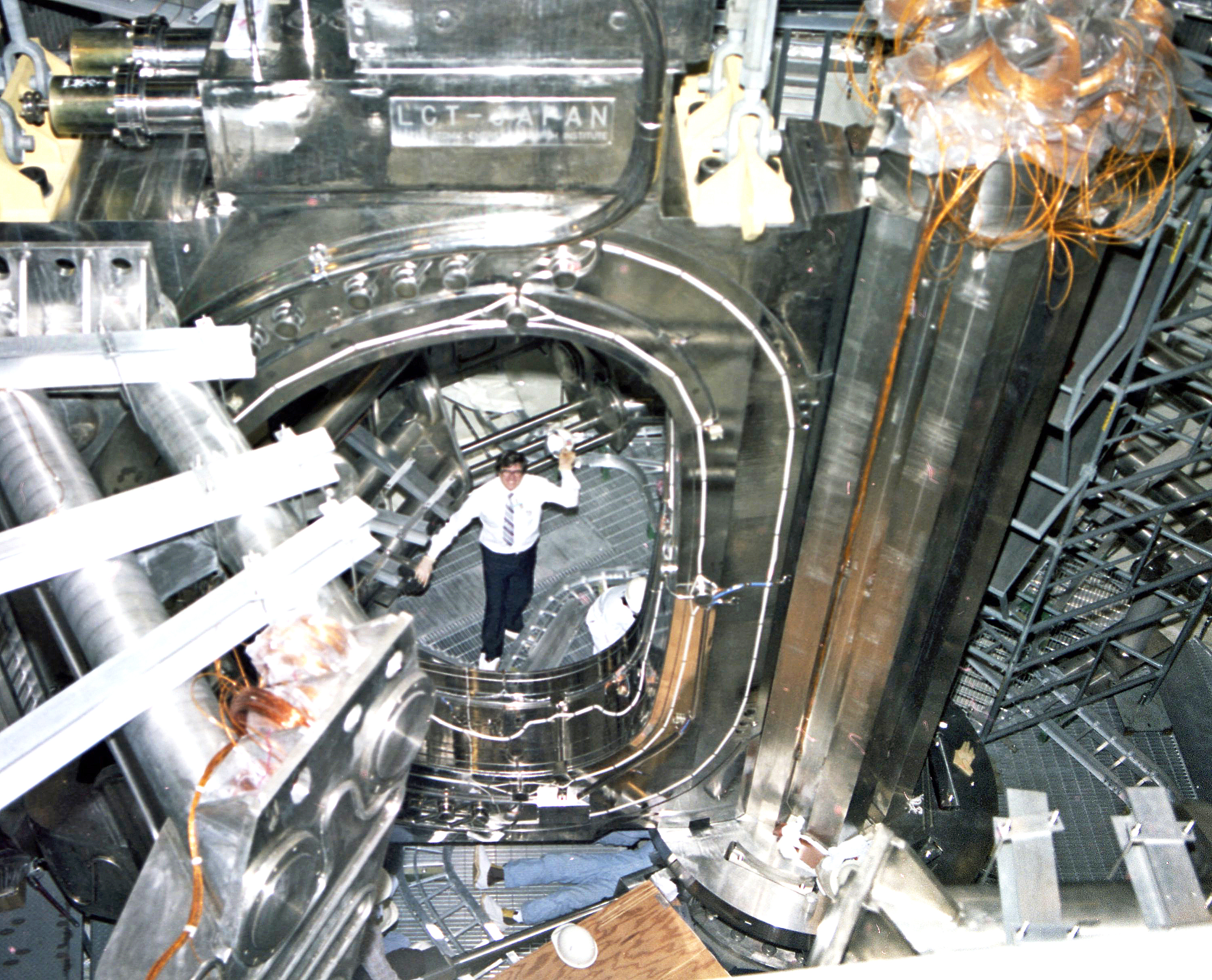 A man standing inside a large magnetic coil, shaped like a flattened oval, inside a large pressure vessel