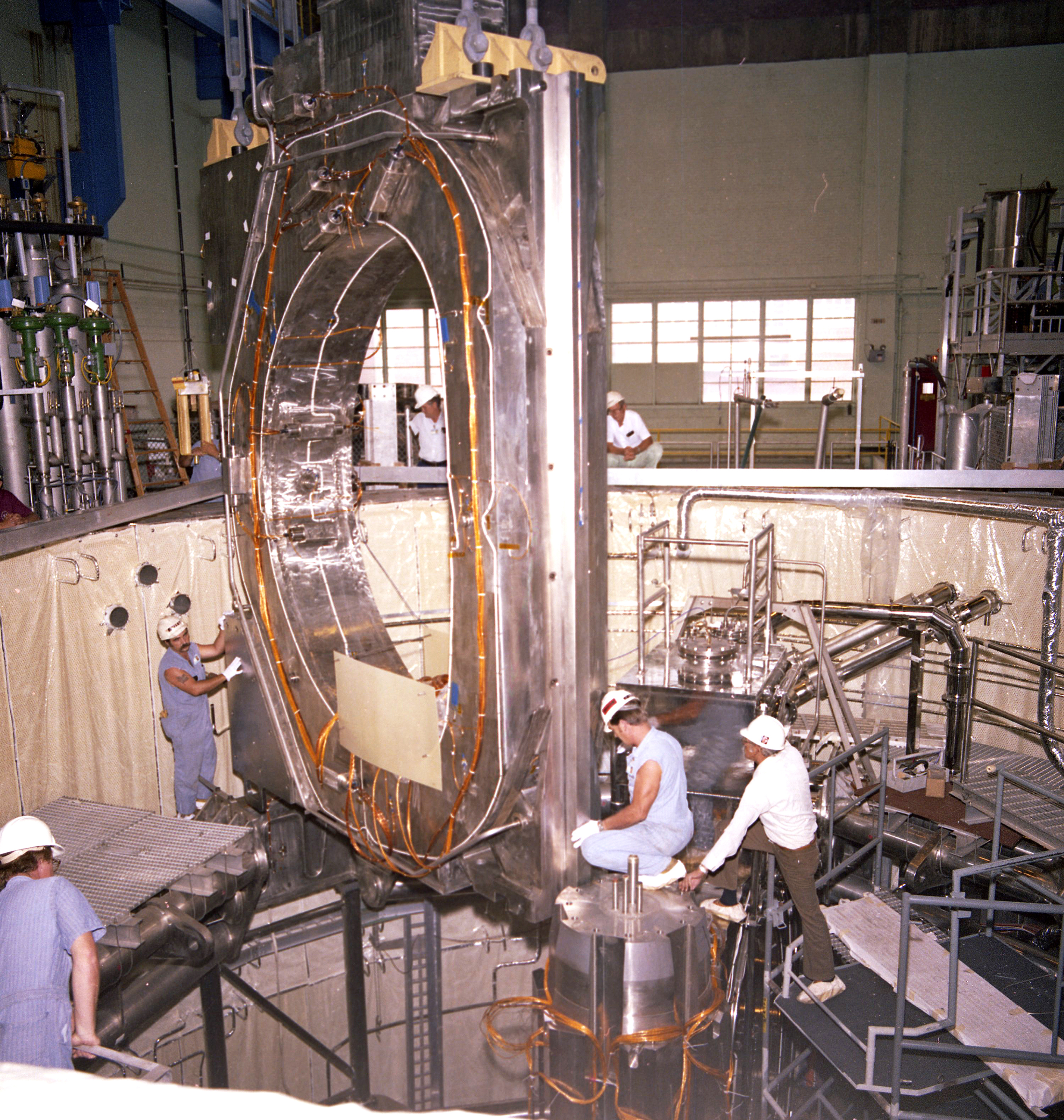 Workers lowering a large magnetic coil into a vessel