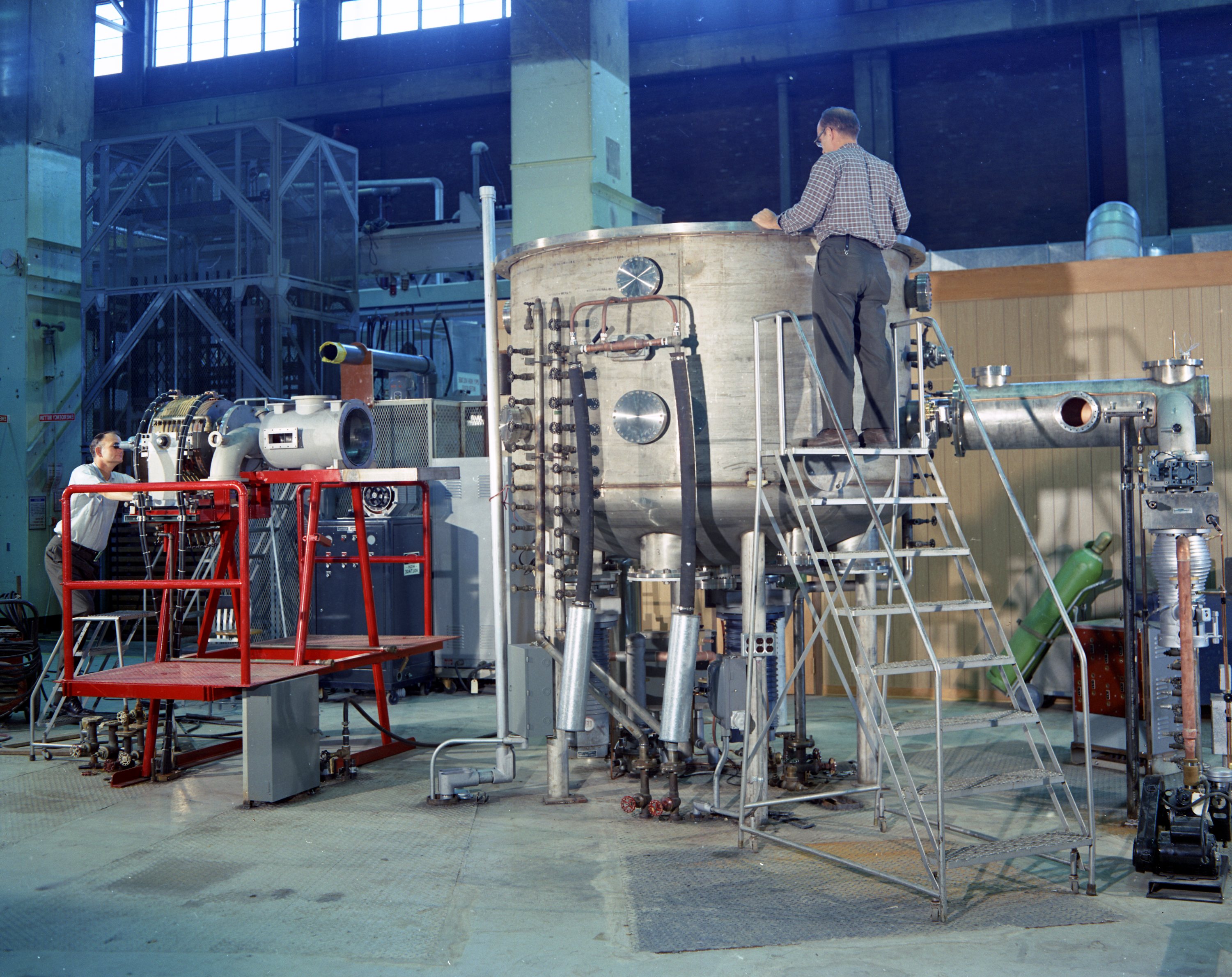 A large metal cylinder with technicians adding scientific equipment to the sides