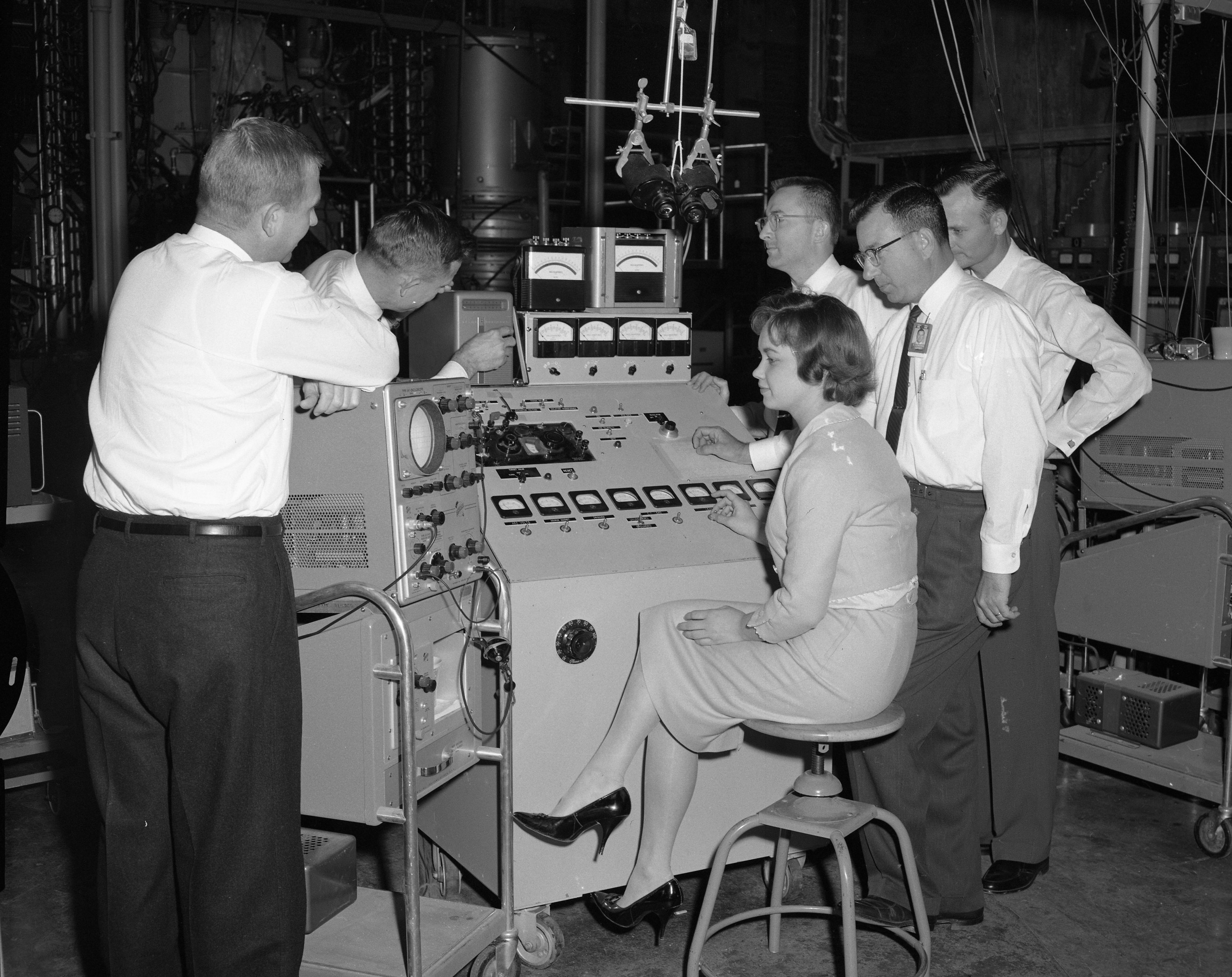 A black and white photo of a group of researchers gathered around an instrument panel for a fusion experiment