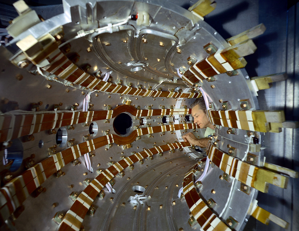 A man performing maintenance inside a small curved tube of a tokamak