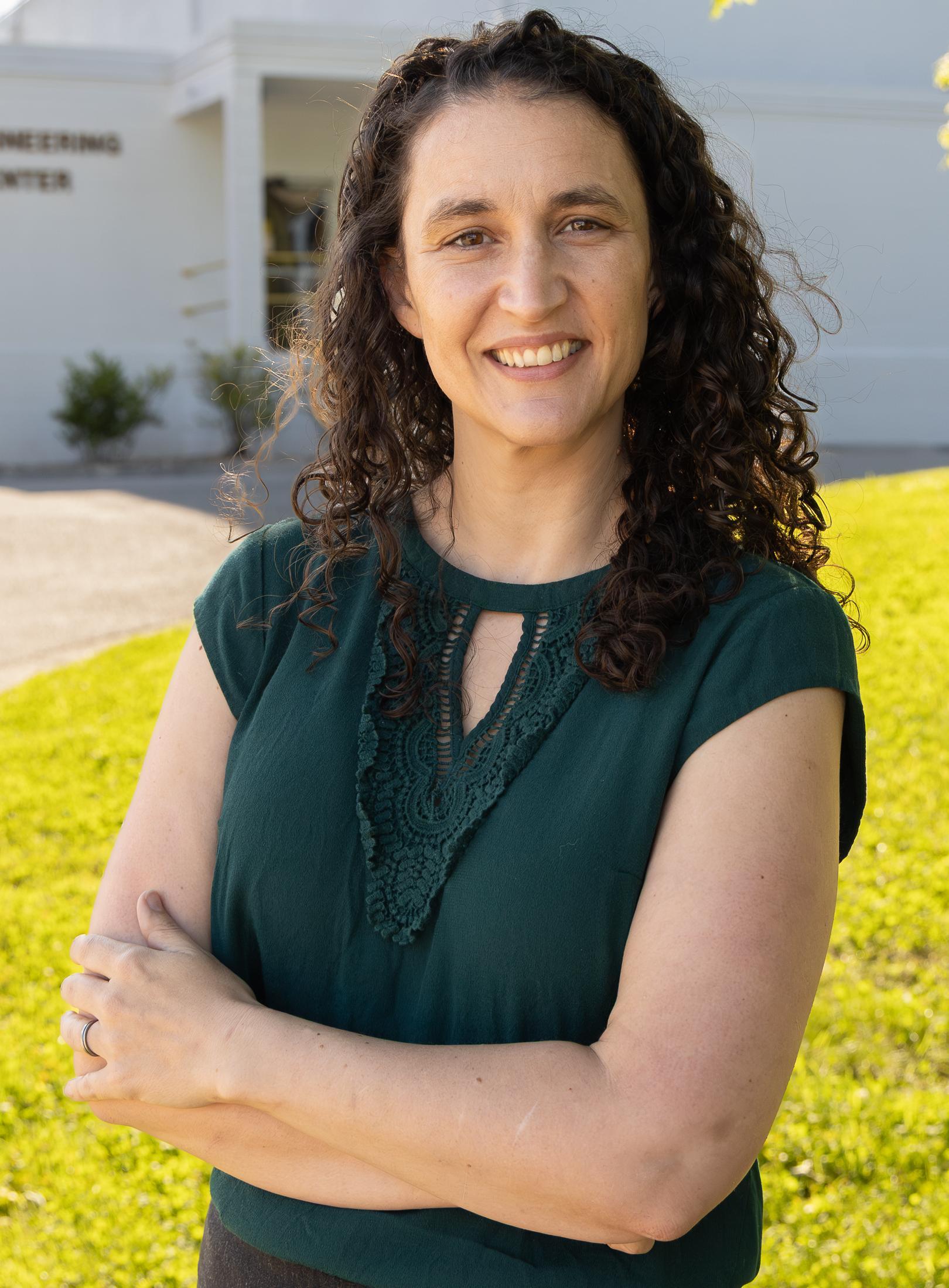 Person smiling in dress clothes stands in front of a white building for a portrait.