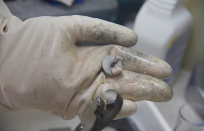 An ORNL researcher holds a test specimen for a study of whether irradiation can slow corrosion of metal in liquid salt. Preliminary experiments seem to indicate that it can. Credit: ORNL, U.S. Dept. of Energy