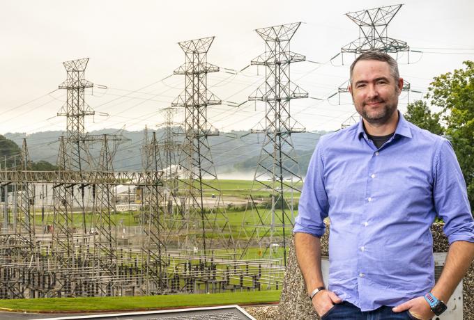 A male researcher stands in front of power lines near a power station