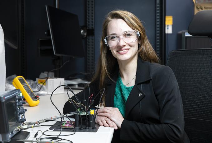A woman in safety glasses smiles while working on microelectronics