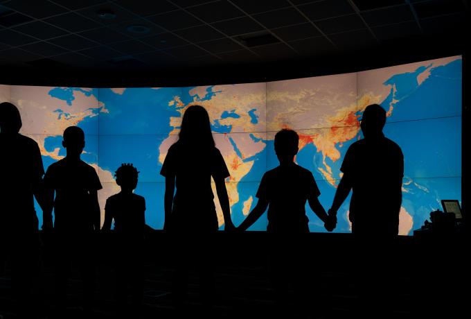 Silhouettes of a family standing in front of world population maps on the EVEREST visualization wall