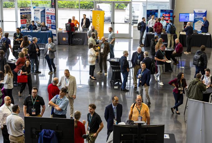 Attendees interact at a busy conference hall with various company booths visible in the background.