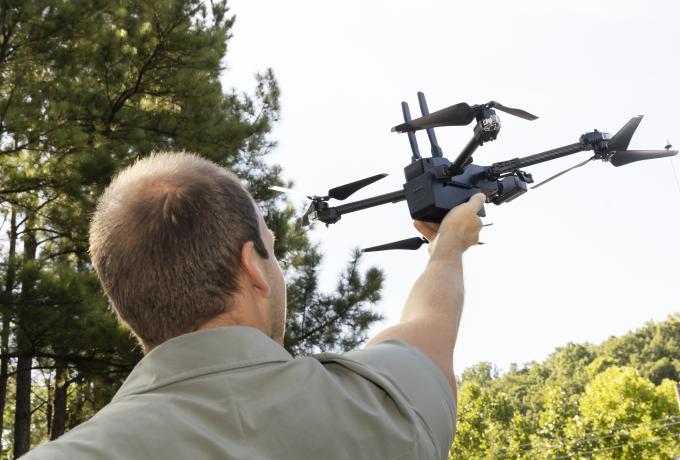 A man in seen from behind as he lifts his arm up to launch a quad copter drone