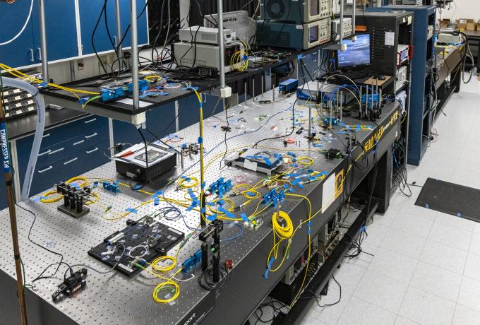Quantum research lab shows bench top work space with detectors and processors connected by yellow wiring