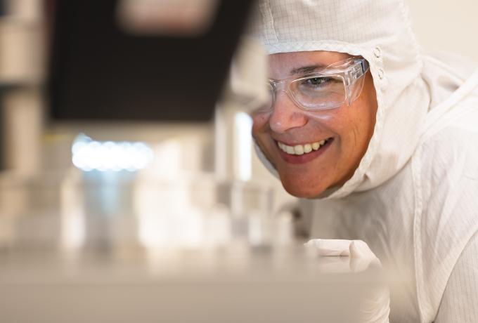 Leslie Wilson, Master Technician in Nanofabrication Research, smiling while looking into a piece of equipment