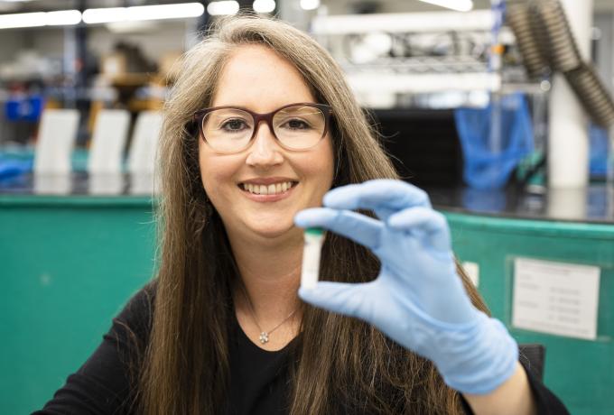 researcher wearing blue latex gloves holds a vial toward the camera