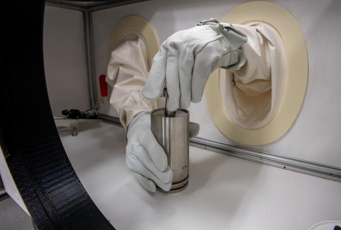 A person handles a canister in a glovebox