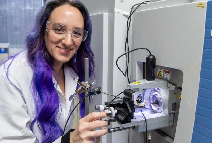 technical professional wearing safety glasses and a lab coat standing next to a mass spectrometer