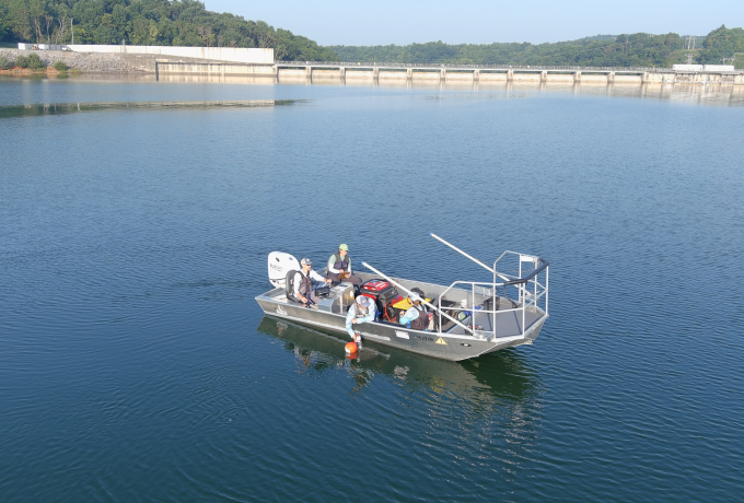 Four researchers in a boat on a lake in front of a dam