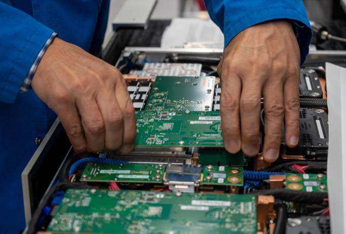 Close-up of a technician's hands installing or adjusting green circuit boards inside a high-performance computing system.