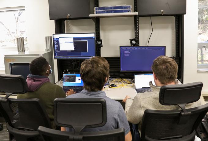 Three men sit side-by-side looking at computer monitors
