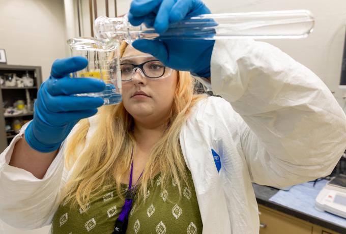 Intern wearing PPE tours liquid between test tubes