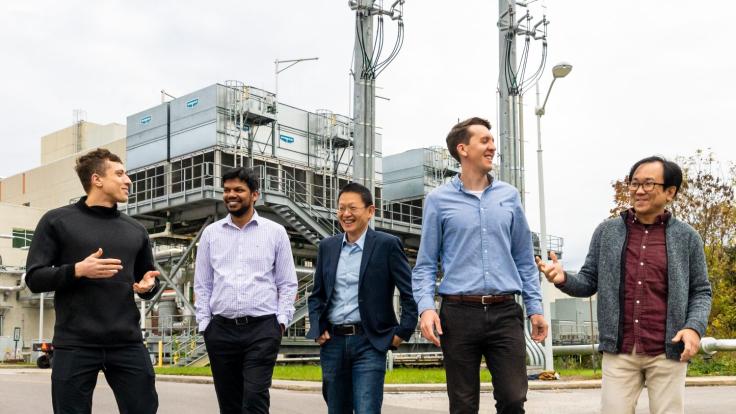 Five men walking toward the camera in front of cooling infrastructure