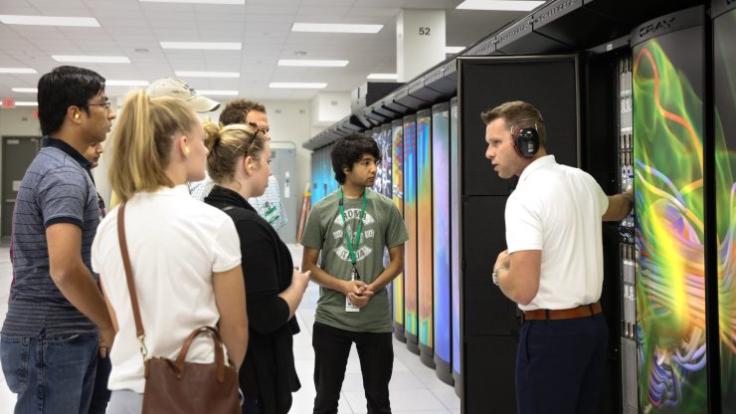 Man in headphones talks to students in front of computer storage system