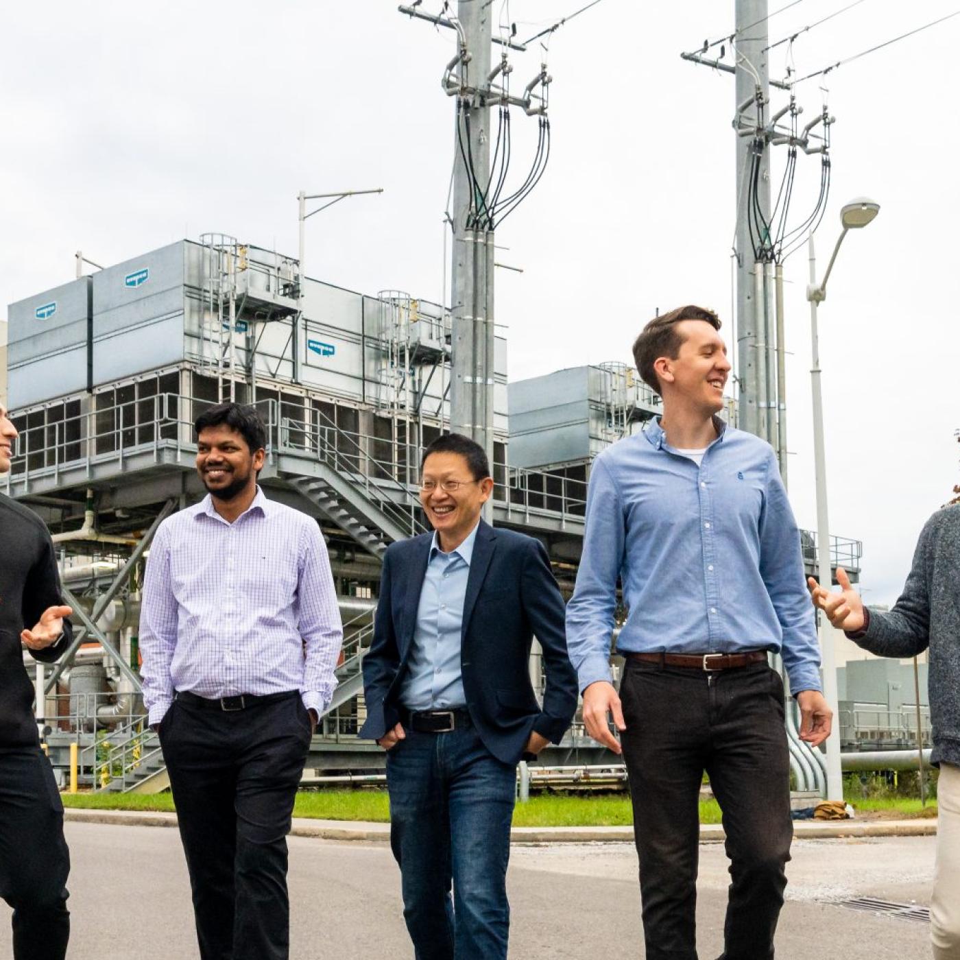 Five men walking toward the camera in front of cooling infrastructure