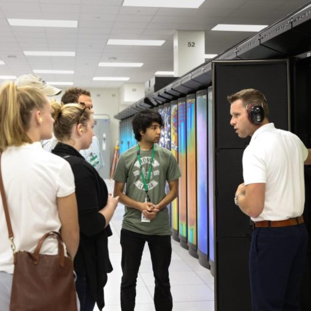 Man in headphones talks to students in front of computer storage system