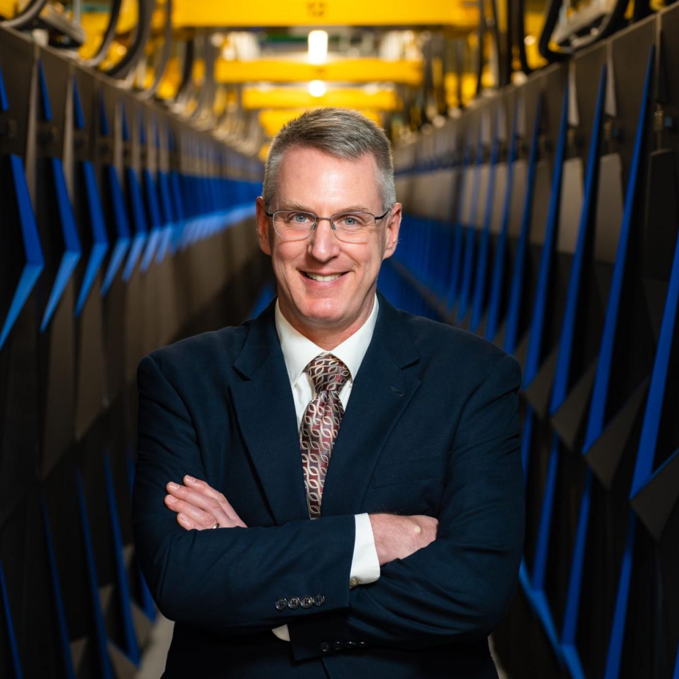 Portrait of Phil Roth standing between cabinets of the Summit supercomputer