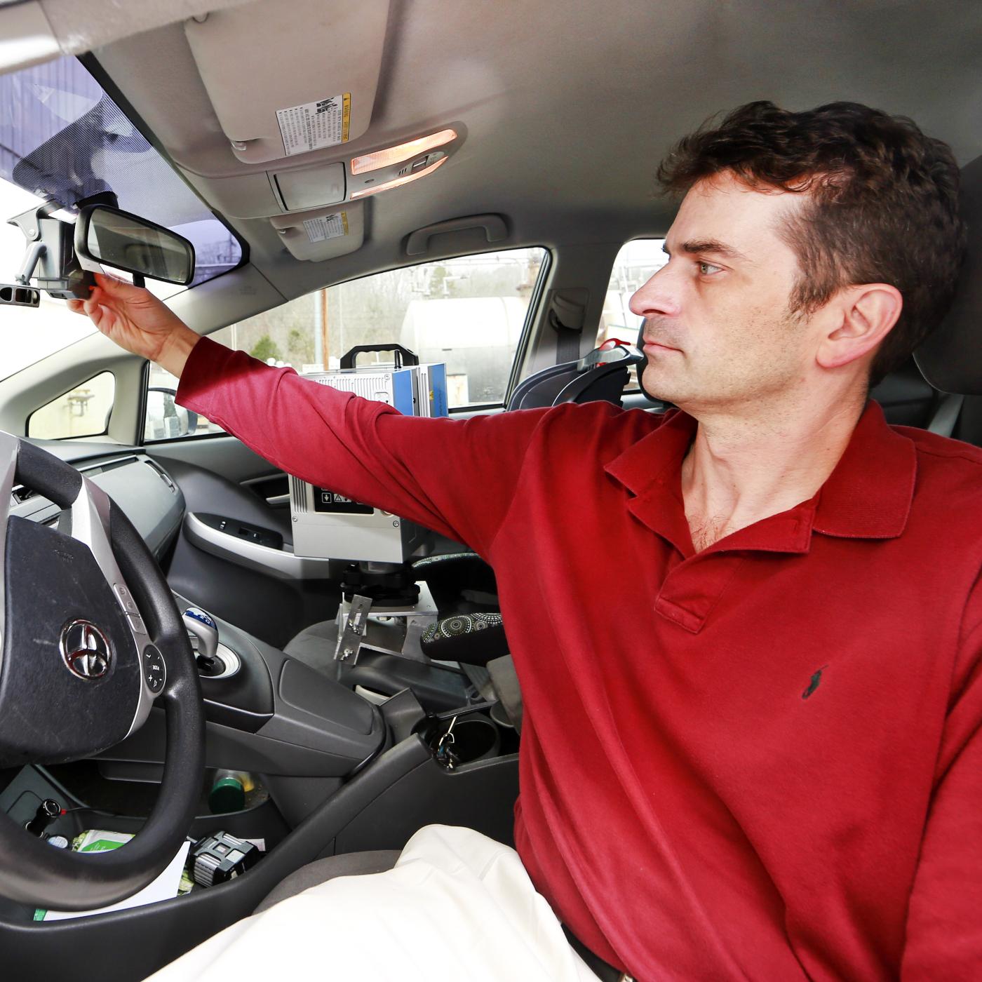 Tom Karnowski sits in the drivers seat of a car and adjusts a sensor behind the rear view mirror