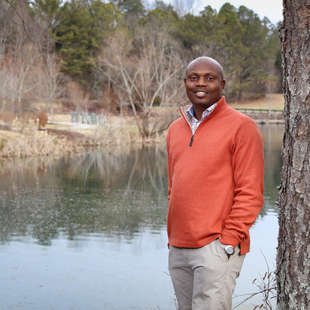 Stephen Dahunsi poses for a picture by a tree near a pond
