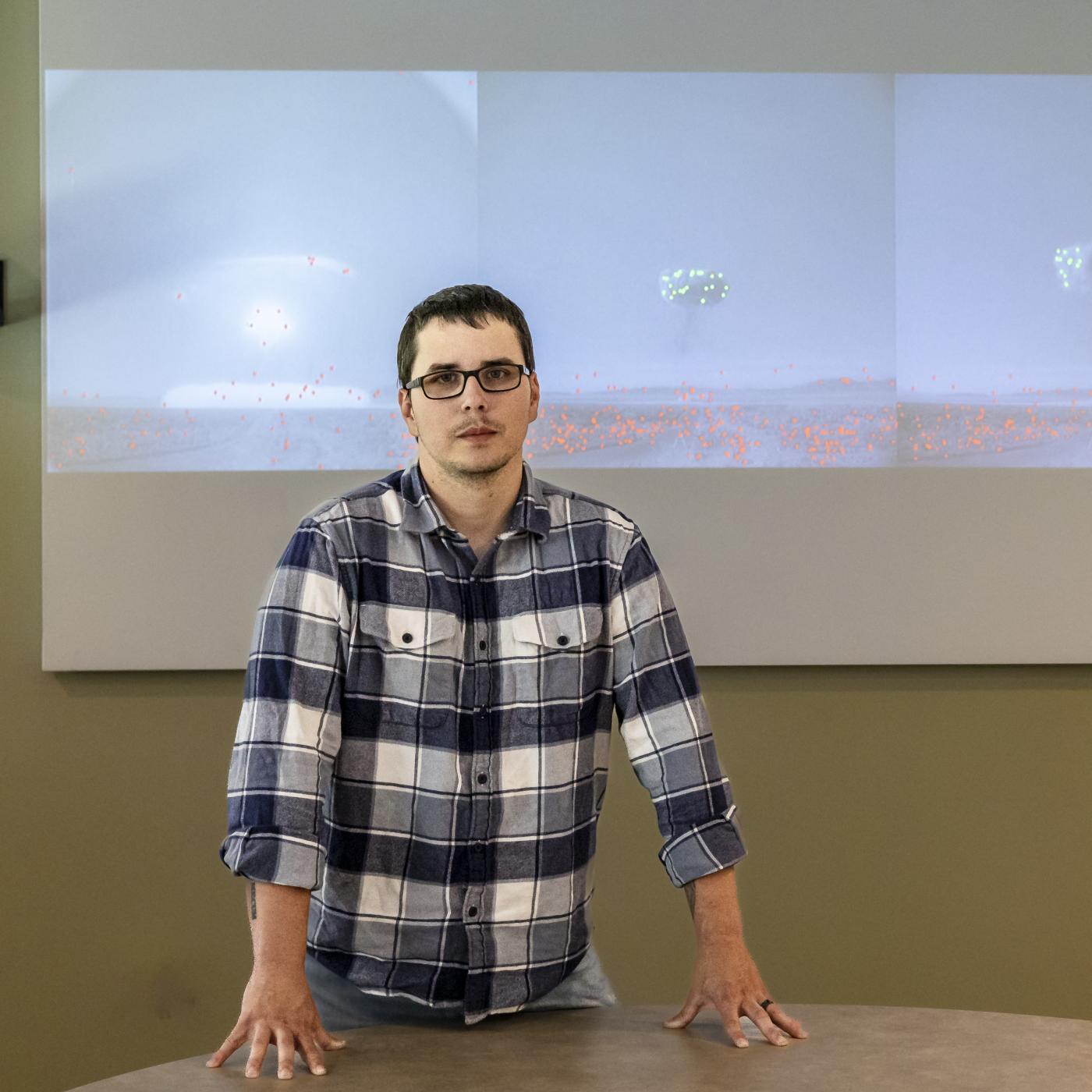 Cody Lloyd stands in front of images of historical nuclear field testing. The green and red dots are the machine learning algorithm recognizing features in the image. Credit: Carlos Jones/ORNL, U.S. Dept. of Energy