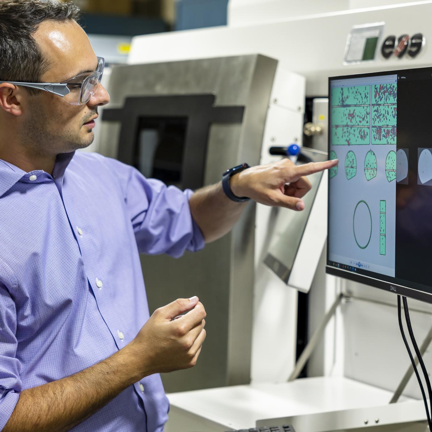 ORNL researcher Zackary Snow compares data from different types of images collected during and after metal parts were additively manufactured using a powder bed printer like the one behind him. Credit: Carlos Jones/ORNL, U.S. Dept. of Energy 