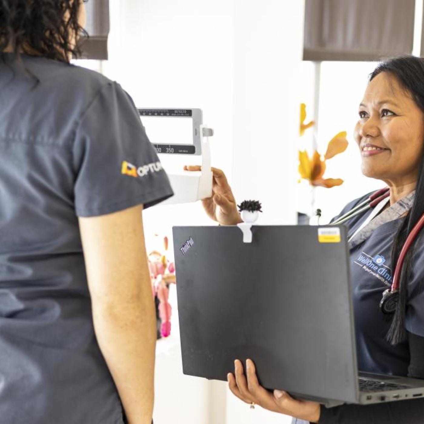 One nurse talks with another nurse while holding a laptop