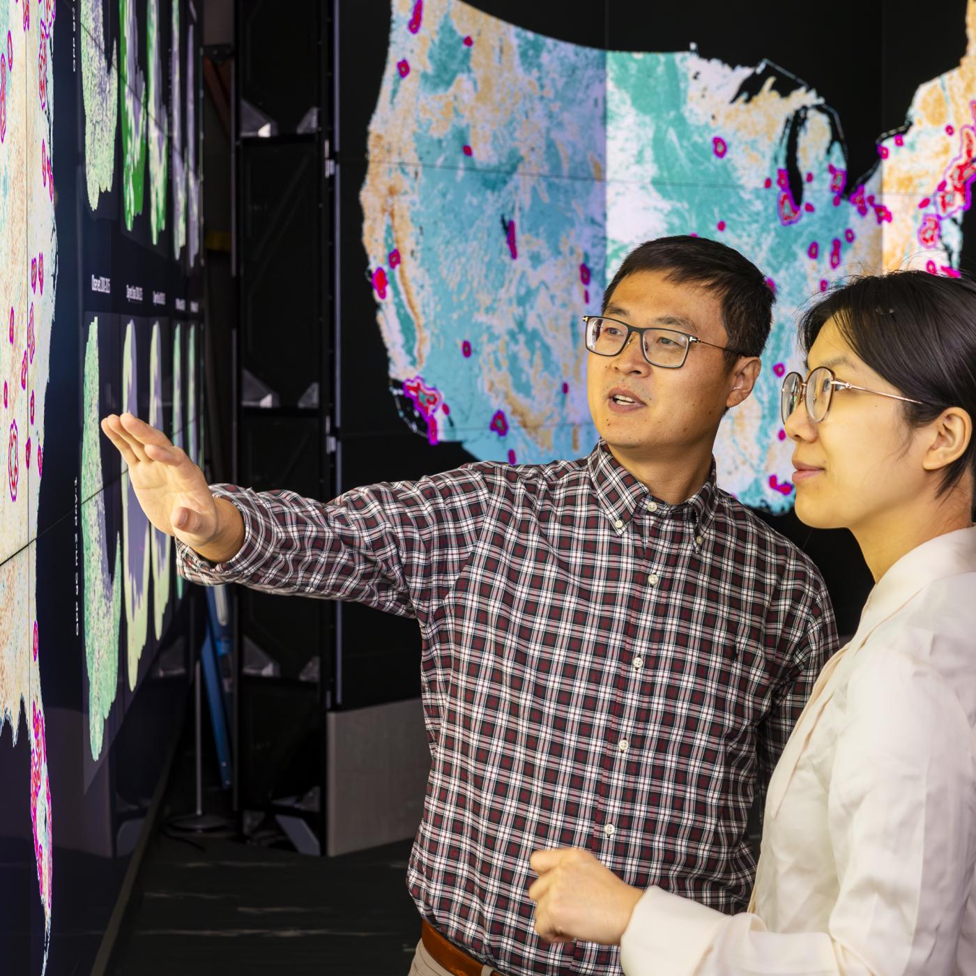 Jiafu Mao, left, and Yaoping Wang discuss their analysis of urban and rural vegetation resilience across the United States in the EVEREST visualization lab at ORNL. Credit: Carlos Jones, ORNL/U.S. Dept. of Energy