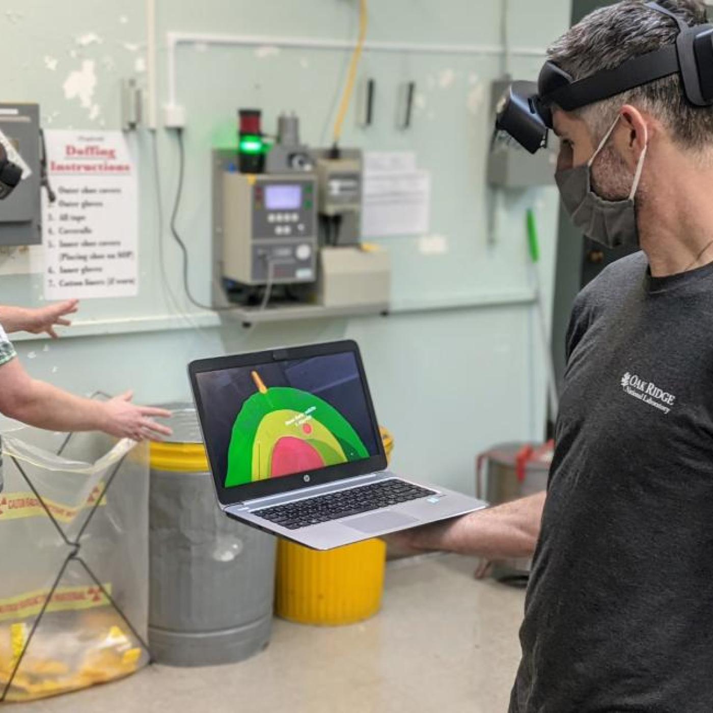 ORNL inventor Michael Smith, right, holds a laptop showing what Scott Greenwood, left, sees through an augmented reality headset. 