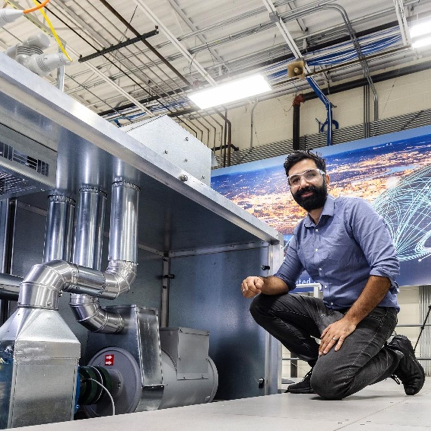Researcher Maximiliano Ferrari is kneeling down next to an emulator in the networked microgrids laboratory at the Grid Research Integration and Deployment Center