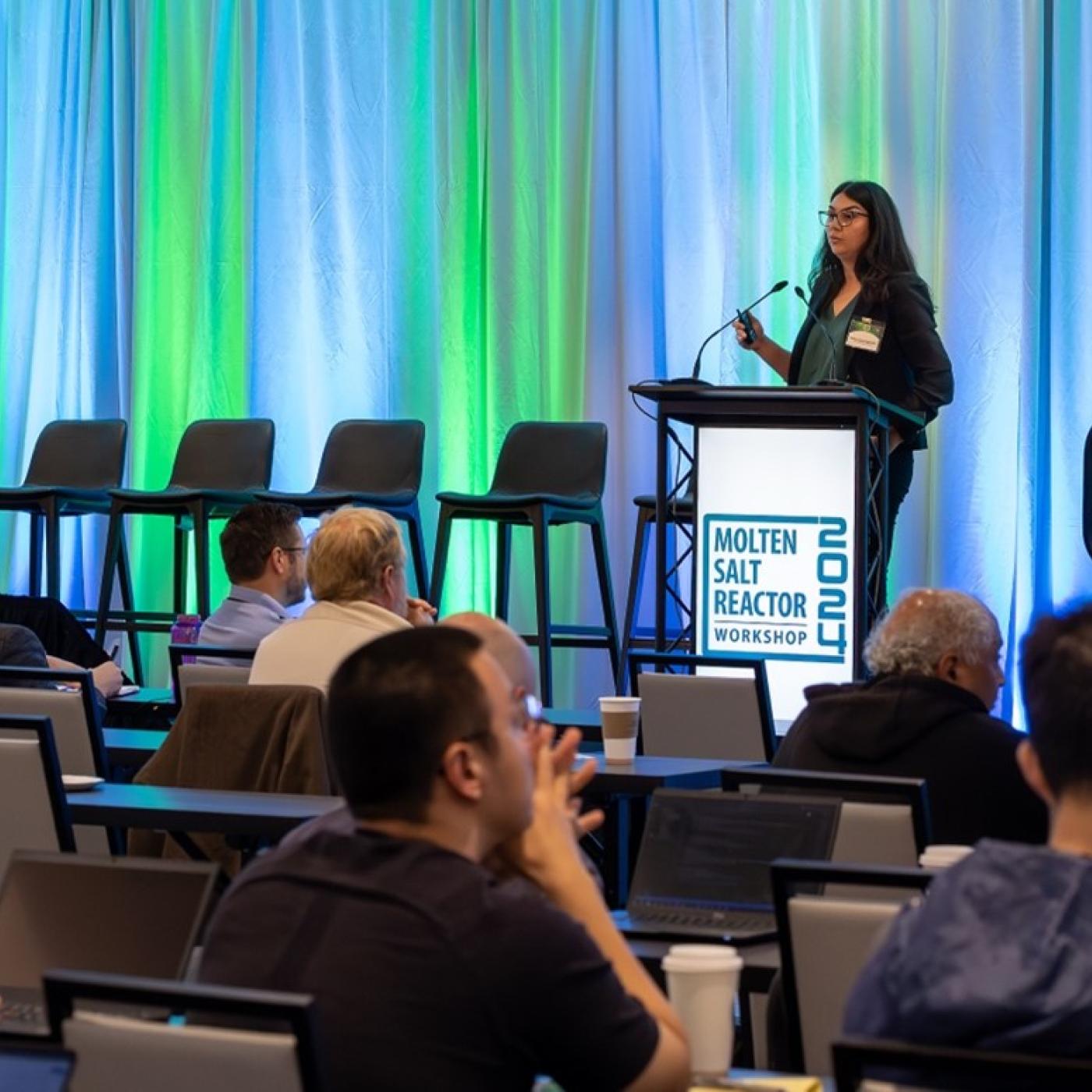 ORNL’s Askin Guler Yigitoglu presents during the 2024 Molten Salt Reactor Workshop in Knoxville with a green and blue background