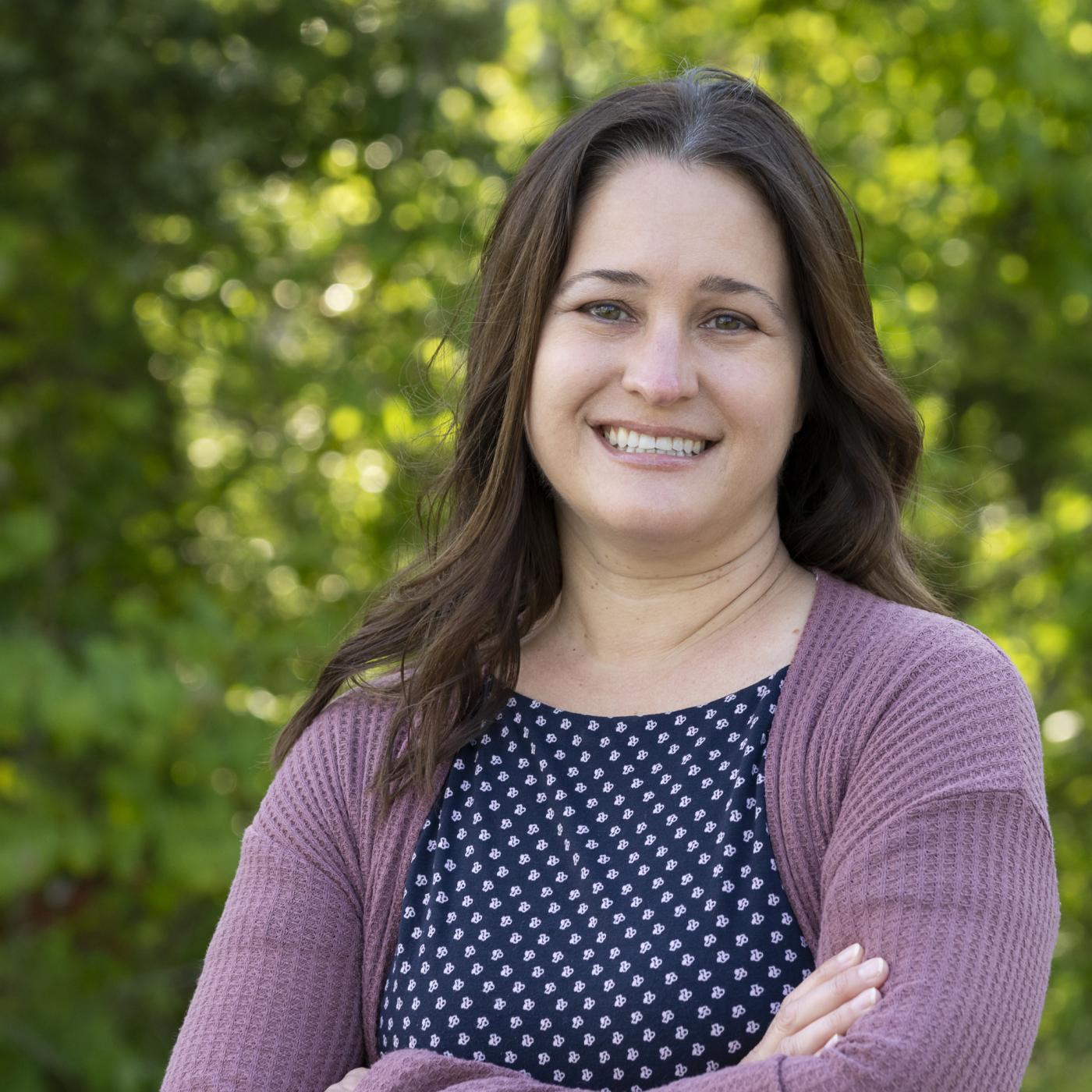 ORNL researcher Melissa Cregger is standing outside smiling for a photo. Woman is wearing blue and white polka dot shirt with a purple cardigan. 
