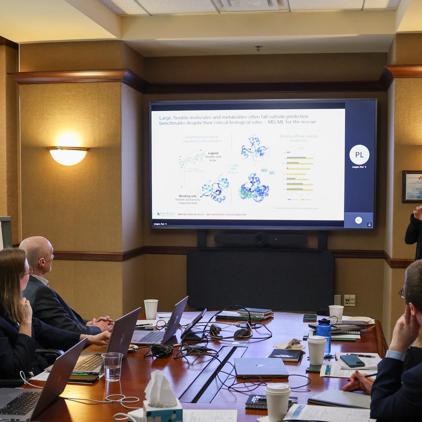 Erica Prates is presenting to a group of attendees at Vandy workshop in a table conference room, standing next to a screen glowing in white