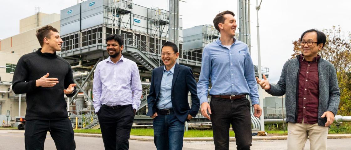 Five men outside in front of a industrial cooling towers