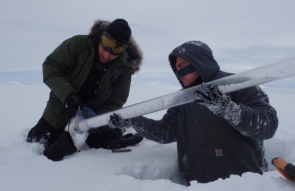 Two men waist deep in snow collecting samples.