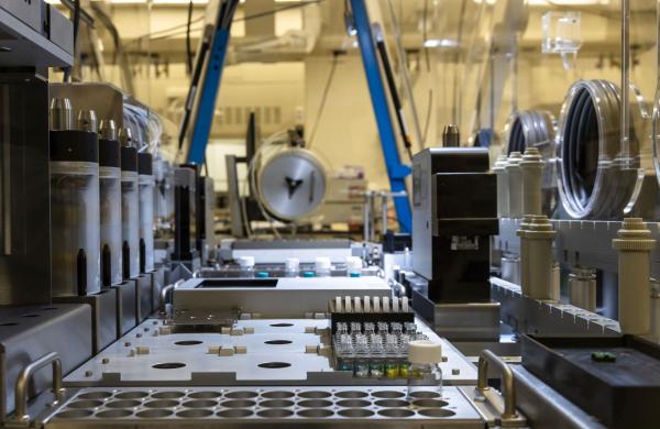 Robotic chemistry lab with glass material jars off to the right and two blue pillars in the background