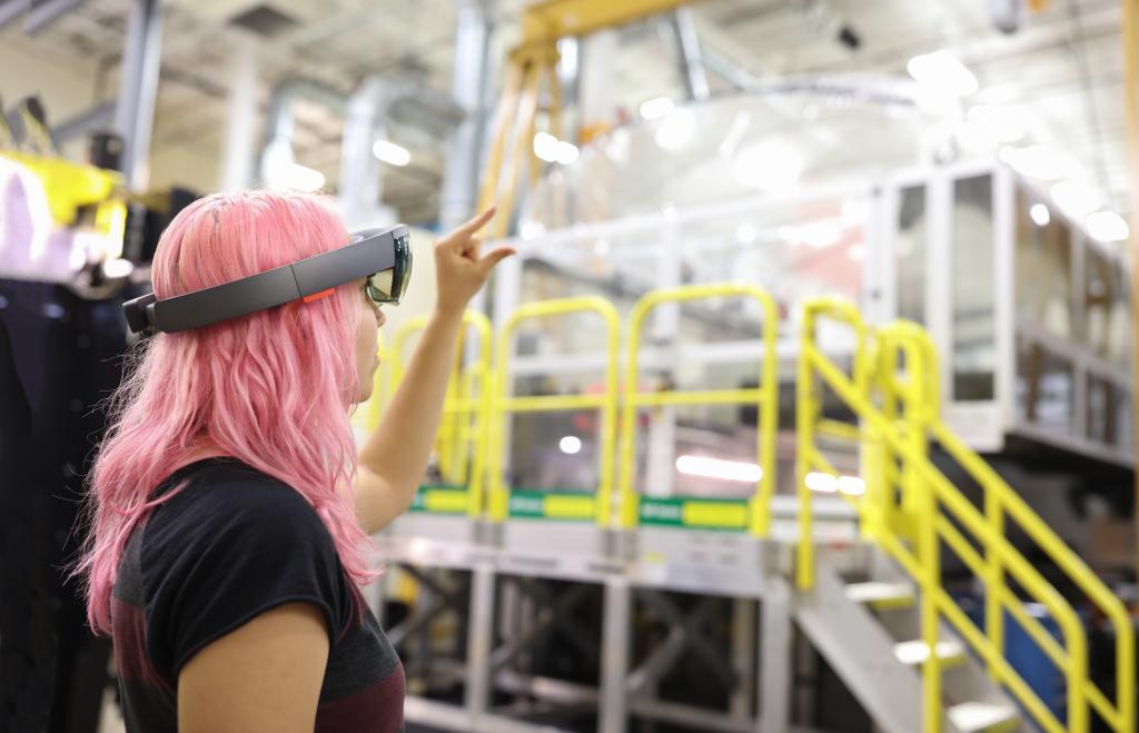 artificial intelligence for manufacturing, woman with pink hair standing in manufacturing high bay with VR glasses on.