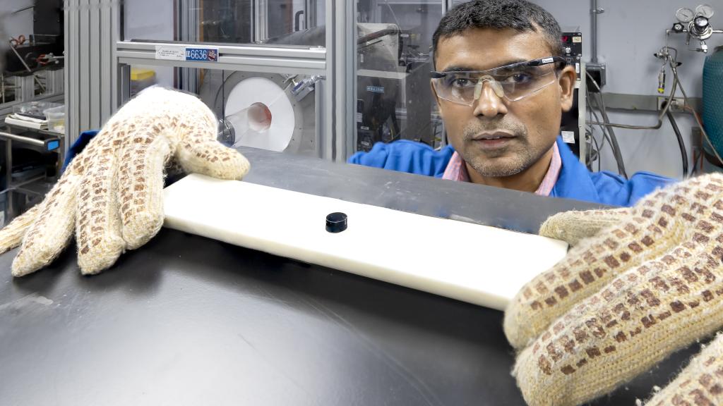 Chanaka Kumara of ORNL used a chemical vapor deposition system, in the background, to coat a stainless-steel disc, in the foreground, with carbon nanotubes. 