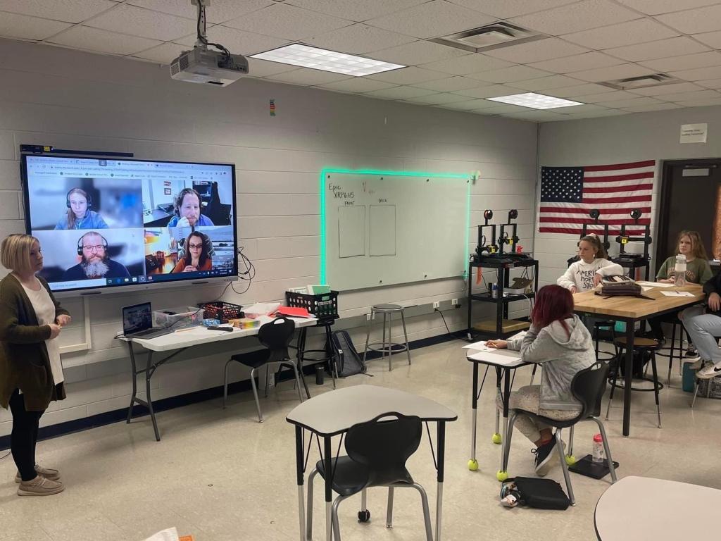 Students sitting at desks looking at monitor with scientists who joined remotely.