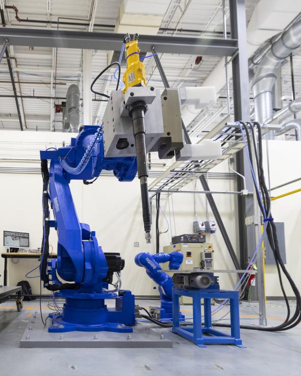 Blue robot arm, taller than a man, with screwdriver attachment, in a multi-story lab