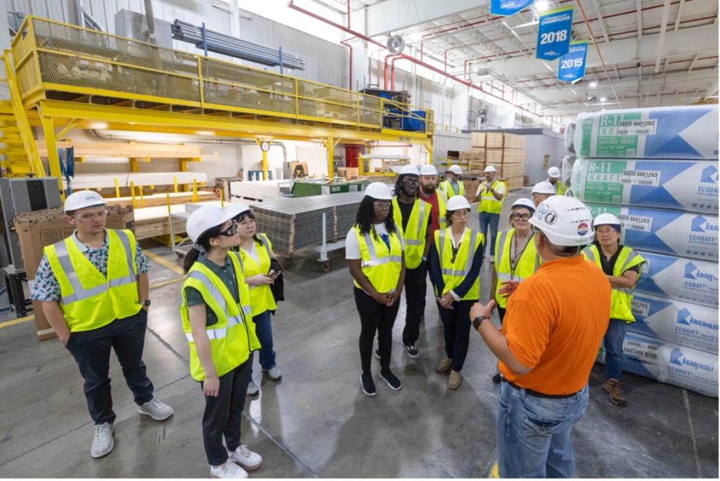 group of people in an industrial building wearing safety vests and white hard hats