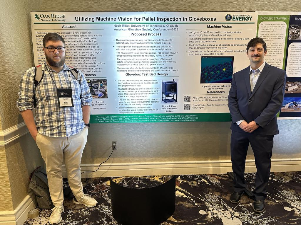 Intern Noah Miller, left, and his mentor, Joe McVeigh, stand with their poster at the American Glovebox Society conference in 2023.